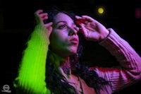 a woman is holding her head up in front of a neon light