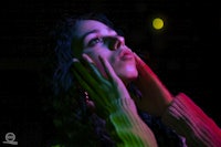 a woman is holding her hand up in front of a colorful light