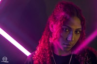 a woman with curly hair in front of a neon light