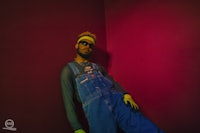 a man in overalls leaning against a wall