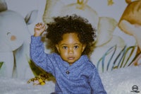 a baby boy is sitting on a blanket with a giraffe in the background