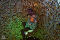 a man sitting on a stool in front of a wall covered in stickers